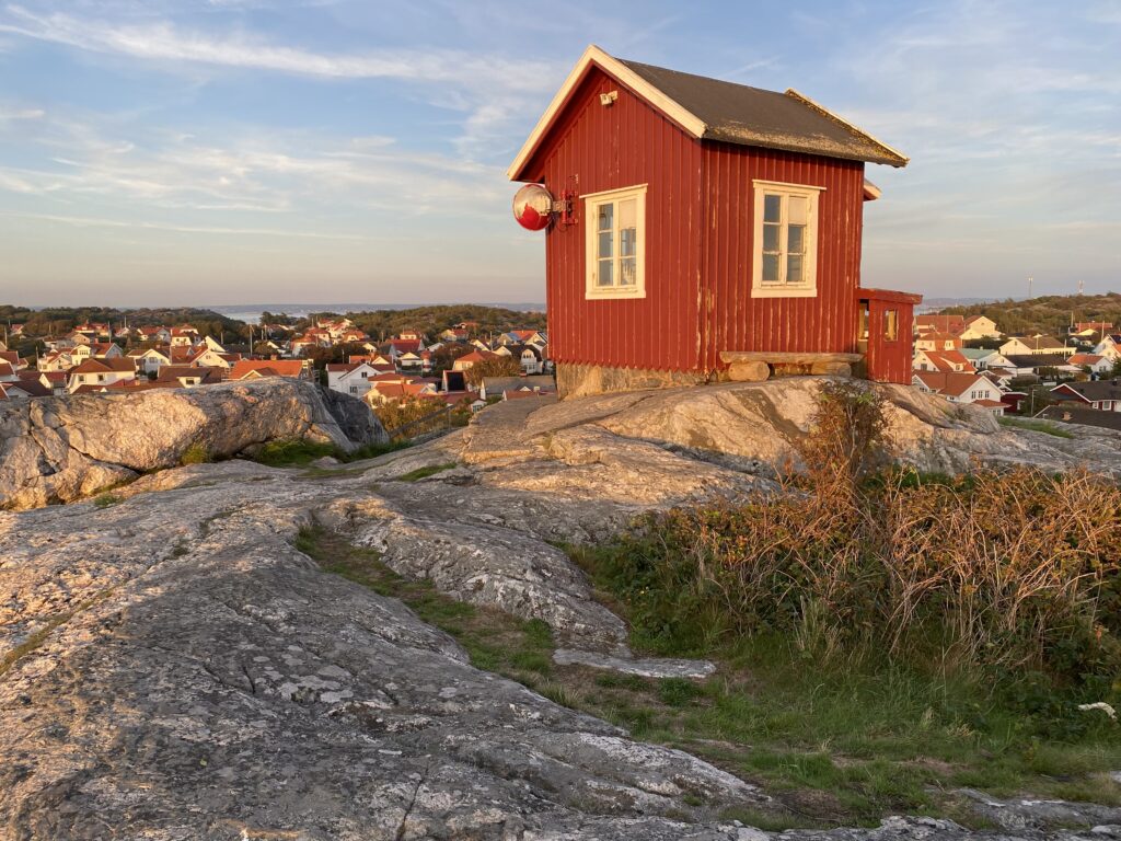Foto som visar röd liten stuga, Utkiken på Vrångö i Göteborgs skärgård. I bakgrunden stugor.